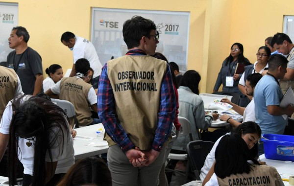 An observer of the Organization of American States (OAS) looks on as members of Honduras' Supreme Electoral Tribunal (TSE) count votes in Tegucigalpa, on December 9, 2017 two weeks after the presidential election. Honduras's leftwing opposition is demanding a presidential election held two weeks ago be voided and its results annulled, alleging it was 'rigged' in favor of incumbent President Juan Orlando Hernandez. The Alliance Against the Dictatorship coalition backing Hernandez's chief rival in the poll, Salvador Nasralla, lodged the demand late Friday with the Supreme Electoral Tribunal. / AFP PHOTO / Orlando SIERRA