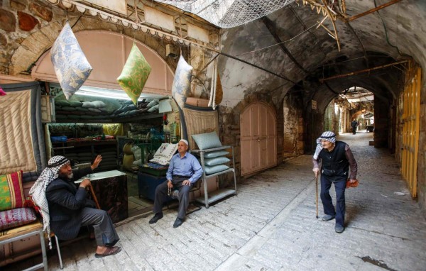 A Palestinian man walks by another two sitting outside a cushion shop in the old market of the divided West Bank city of Hebron on July 7, 2017.On July 7, 2017 UNESCO declared in a secret ballot the Old City of Hebron in the occupied West Bank a protected heritage site.Hebron is home to more than 200,000 Palestinians, and a few hundred Israeli settlers who live in a heavily fortified enclave near the site known to Muslims as the Ibrahimi Mosque and to Jews as the Cave of the Patriarchs. / AFP PHOTO / HAZEM BADER
