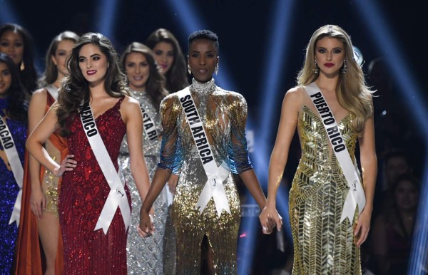 (L-R) Miss Mexico Sofia Aragon, Miss South Africa Zozibini Tunzi and Miss Puerto Rico Madison Anderson hold hands on stage during the 2019 Miss Universe pageant at the Tyler Perry Studios in Atlanta, Georgia on December 8, 2019. (Photo by VALERIE MACON / AFP)