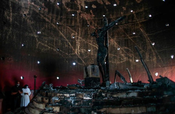 A priest and a nun pray next to the image of 'Christ's Blood' after a fire burnt it at the Cathedral in Managua on July 31, 2020. - The Managua Cathedral was attacked with a molotov bomb by an unknown person damaging an image venerated by the Nicaraguan Catholic faithful. (Photo by Oswaldo RIVAS / POOL / AFP)