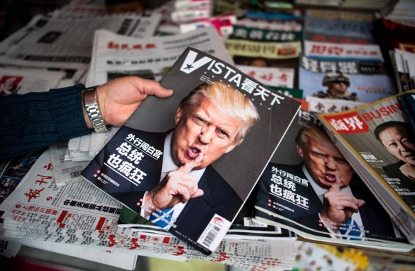 A woman holds a Chinese newspaper with a picture of US President Donald Trump at a news stand in Shanghai on April 5, 2017. / AFP PHOTO / Johannes EISELE