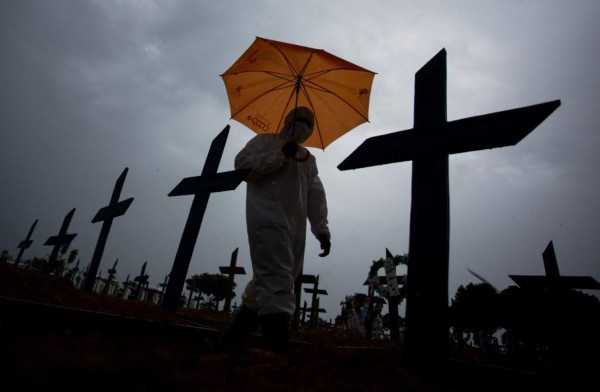 A worker wearing a protective suit and carrying an umbrella walks past the graves of COVID-19 victims at the Nossa Senhora Aparecida cemetery, in Manaus, Brazil, on February 25, 2021. - Brazil surpassed 250,000 deaths due to COVID-19. (Photo by MICHAEL DANTAS / AFP)