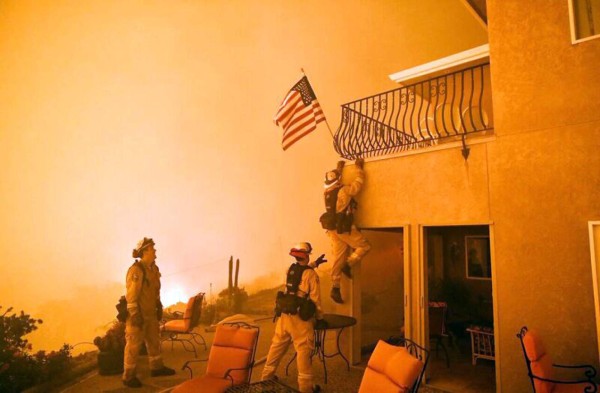 Firefighters save a US flag as impending flames from the Wall fire close in on a luxury home in Oroville, California on July 8, 2017. At least 10 structures have burned and the fire is currently at 20 percent containment.The first major wildfires after the end of California's five-year drought raged across the state on July 8, as it was gripped by a record-breaking heatwave. / AFP PHOTO / JOSH EDELSON