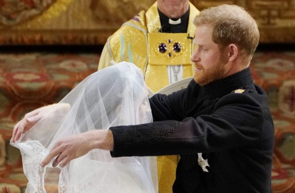 Britain's Prince Harry, Duke of Sussex (R) removes the veil of US actress Meghan Markle (L) as they stand at the altar together before Archbishop of Canterbury Justin Welby (C) in St George's Chapel, Windsor Castle, in Windsor, on May 19, 2018 during their wedding ceremony. / AFP PHOTO / POOL / Owen Humphreys