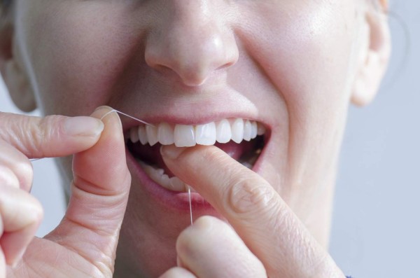 Close up of woman no makeup using dental floss seen from front with white background