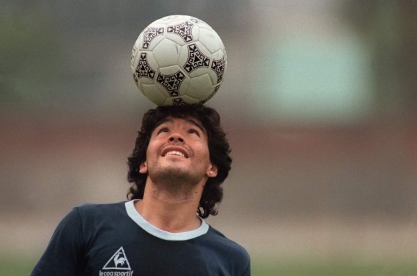 (FILES) In this file photo taken on May 22, 1986 Argentine football star Diego Maradona, wearing a diamond earring, balances a soccer ball on his head as he walks off the practice field following the national selection's practice session in Mexico City. - Argentinian football legend Diego Maradona passed away on November 25, 2020. (Photo by JORGE DURAN / AFP)