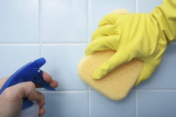 Cleaning shower tile with a sponge and spray bottle of cleaner