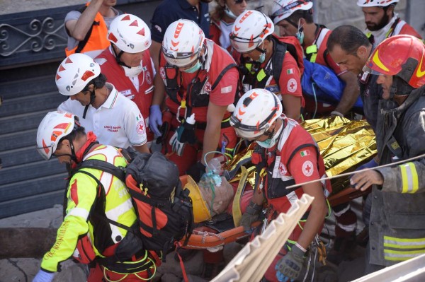 Rescue and emergency services personnel carry a survivor on a stretcher during search and rescue operations in Amatrice on August 24, 2016 after a powerful earthquake rocked central Italy. A powerful earthquake rattled a remote area of central Italy, leaving at least 120 people dead and and some 368 injured amongst scenes of carnage in mountain villages. / AFP PHOTO / FILIPPO MONTEFORTE