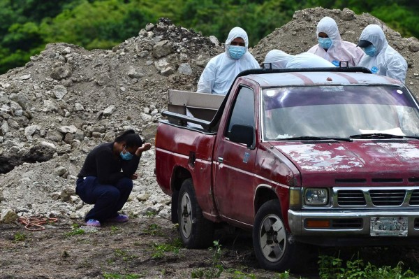 A woman cries as relatives in protective suits unload the coffin of a deceased loved one who died of COVID-19 from a pick-up truck, to bury it in a lot acquired by the Central District Municipal Mayoralty next to the Jardin de Los Angeles cemetery to bury victims of the novel coronavirus, on the outskirts of Tegucigalpa on June 12, 2020. - The pandemic has killed at least 421,691 people worldwide since it surfaced in China late last year, according to an AFP tally at 1100 GMT on Friday, based on official sources. Latin America has become the epicentre of the pandemic with more than 73,600 deaths, over half of which have been in Brazil. (Photo by Orlando SIERRA / AFP)