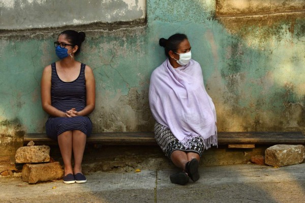 TOPSHOT - Two women wear face masks as a precautionary measure against the spread of the new coronavirus, COVID-19, as they lean against the outside wall of the Thorax Hospital in Tegucigalpa, on April 14, 2020. - The worldwide death toll from the novel coronavirus pandemic rose to 120,013 on Tuesday, according to a tally compiled by AFP at 1100 GMT from official sources. (Photo by Orlando SIERRA / AFP)