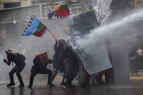 TOPSHOT - Demonstrators protesting against the economic policies of the government of President Sebastian Pinera are sprayed with a water cannon during clashes with riot police in Santiago, on November 4, 2019. - Unrest began in Chile last October 18 with protests against a rise in transport tickets and other austerity measures and descended into vandalism, looting, and clashes between demonstrators and police. Protesters are angry about low salaries and pensions, poor public healthcare and education, and a yawning gap between rich and poor. (Photo by RODRIGO ARANGUA / AFP)