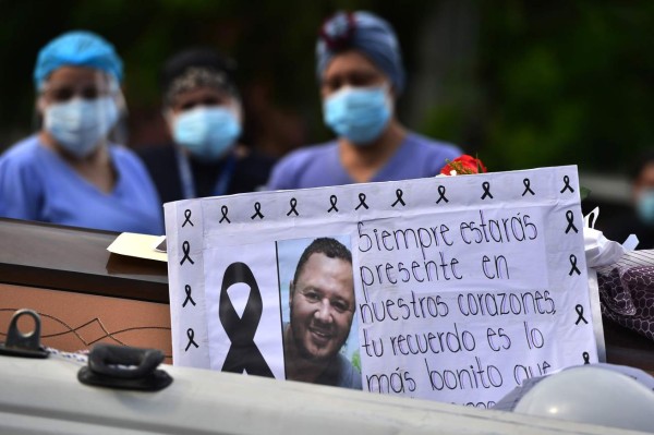 View of a sign reading ?You will always be present in our hearts? as colleagues surround the coffin of a male nurse of the Honduran Institute of Social Security (IHSS), who died from COVID-19, during his funeral in Tegucigalpa, on August 6, 2020. - At least 62 health workers have died in Honduras from the new coronavirus. According to authorities, over 1,400 people have died from the disease in the country from the over 45,000 contagions. (Photo by ORLANDO SIERRA / AFP)
