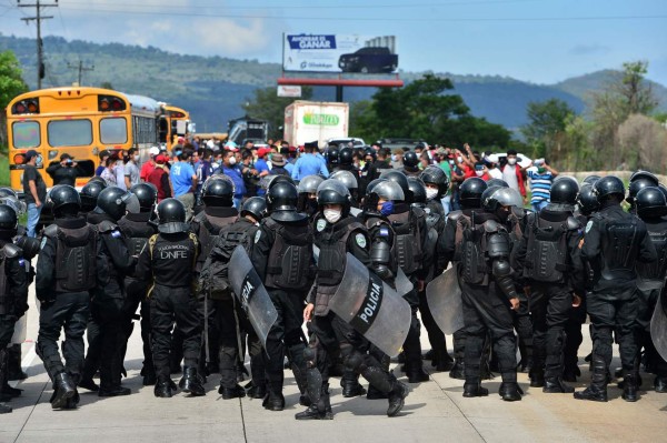 Riot police stand in front of public transport workers who block a highway in demand of aid from the government during a lockdown imposed against the spread of the new coronavirus, 5 km south of Tegucigalpa, on May 21, 2020. - Drivers and conductors assure they have not been able to work in the last 70 days. Accoring to official reports 3,100 people have been infected and 151 have died from COVID-19 in Honduras so far. (Photo by ORLANDO SIERRA / AFP)