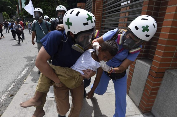 A person affected by the tear gas shot by riot police during a protest by opposers is carried away by volunteer medics in Caracas, on May 24, 2017Venezuela's President Nicolas Maduro formally launched moves to rewrite the constitution on Tuesday, defying opponents who accuse him of clinging to power in a political crisis that has prompted deadly unrest. / AFP PHOTO / JUAN BARRETO