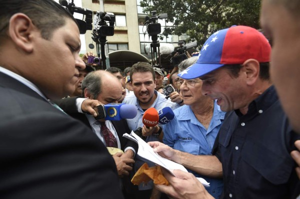 Venezuelan opposition leader and Miranda state Governor Henrique Capriles (R) hands a document to National Electoral Council member Luis Rondon Gonzalez (L) in Caracas on May 18, 2016. Public outrage over sweeping new emergency powers decreed this week by President Nicolas Maduro was expected to spill onto the streets of Venezuela Wednesday, with planned nationwide protests marking a new low point in his unpopular rule. / AFP PHOTO / JUAN BARRETO