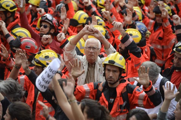 TOPSHOT - Protesters joined by firefighters raise their hands as they gather during a general strike in Barcelona called by Catalan unions on October 3, 2017.Large numbers of Catalans are expected to observe a general strike today to condemn police violence at a banned weekend referendum on independence, as Madrid comes under growing international pressure to resolve its worst political crisis in decades. / AFP PHOTO / Josep LAGO