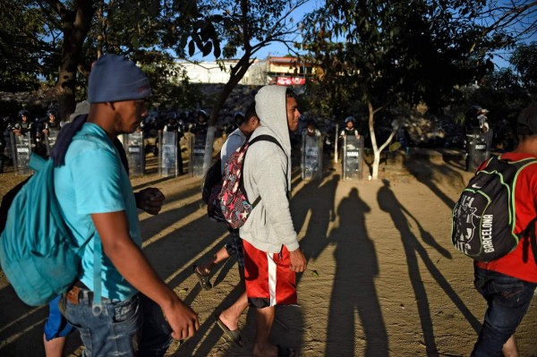 Central American migrants -heading in a caravan for the US- walk past a line of Mexican police on the bank of the Suichate River, where they spent the night, in Ciudad Hidalgo, Mexico, after crossing from Tecum Uman, Guatemala, on January 21, 2020. - Some 500 Central Americans, from the so-called '2020 Caravan', crossed Monday from Guatemala to Mexico, but over 400 were intercepted when National Guardsmen fired tear gas at them. (Photo by ALFREDO ESTRELLA / AFP)