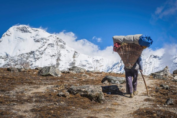 Lukla, Nepal - 25th October 2010: Sherpa porter carrying heavy load of expedition kit in a traditional wicker basket along a rocky trail deep in the mountain wilderness of the Sagarmatha National Park, Himalayas, Nepal.