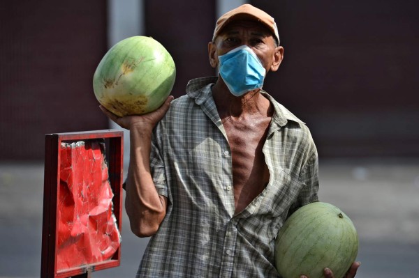 A man wears a face mask against the spread of the new coronavirus as he offers watermelons for sale at a street market in Tegucigalpa, on March 22, 2020. - Authorities have confirmed 26 cases of COVID-19 in the country so far. (Photo by ORLANDO SIERRA / AFP)