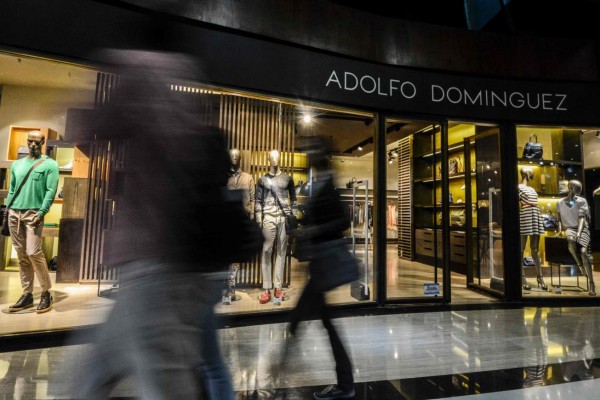 Shoppers walk past a clothing store in a mall in Caracas, Venezuela on May 25, 2017.Venezuela is stricken by poverty and political violence, but a rich minority act as if they were untouched by the crisis. While many struggle to buy food, some are still eating sushi and sipping cocktails in discos and night clubs. / AFP PHOTO / LUIS ROBAYO / TO GO WITH AFP STORY