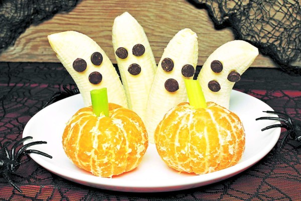 Healthy Halloween treats, banana ghosts and orange pumpkins, on a plate with holiday decor