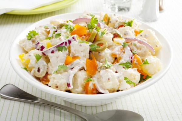 A bowl of potato salad with creamy mustard dressing. Salad also includes orange and yellow peppers, red onions and stuffed olives.