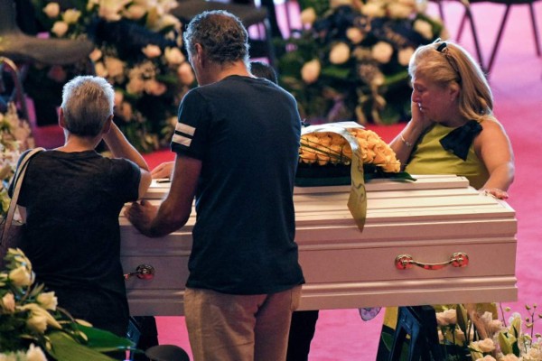 Relatives mourn near the coffins of some of the victims of the collapsed Morandi highway bridge, laid in front of the altar, prior to the start of the funeral service, in Genoa, on August 18, 2018.Fury is growing over the shock collapse of the Morandi bridge, a decades-old viaduct that crumbled in a storm on August 14 killing at least 38 people, with Italian media reporting that some outraged families would shun August 19's official commemorations. / AFP PHOTO / Piero CRUCIATTI