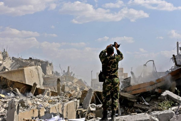 A Syrian soldier inspects the wreckage of a building described as part of the Scientific Studies and Research Centre (SSRC) compound in the Barzeh district, north of Damascus, during a press tour organised by the Syrian information ministry, on April 14, 2018.The United States, Britain and France launched strikes against Syrian President Bashar al-Assad's regime early on April 14 in response to an alleged chemical weapons attack after mulling military action for nearly a week. Syrian state news agency SANA reported several missiles hit a research centre in Barzeh, north of Damascus, 'destroying a building that included scientific labs and a training centre'. / AFP PHOTO / LOUAI BESHARA