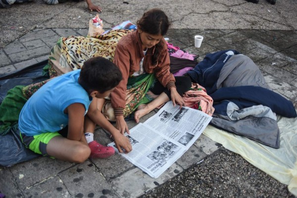 Honduran migrant children taking part in a caravan heading to the US, read a newspaper as they rest at the main square in Tapachula, Chiapas state, Mexico, on October 22, 2018. - President Donald Trump on Monday called the migrant caravan heading toward the US-Mexico border a national emergency, saying he has alerted the US border patrol and military. (Photo by Johan ORDONEZ / AFP)