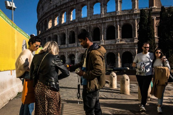 A street seller (C) hands an object to tourists by the closed Colosseum monument in Rome, as Italian government approved drastic measures in an attempt to halt the spread of the COVID-19 outbreak, caused by the novel coronavirus that is sweeping the globe. - Italy on March 8, 2020, had the second-highest coronavirus toll in the world, after reporting a sharp jump in both deaths and number of infected people, according to an AFP count. The number of fatalities shot up by 133 to 366 Sunday, while the number of infections rose by a single-day record of 1,492 to hit 7,375, its civil protection agency said. (Photo by Laurent EMMANUEL / AFP)