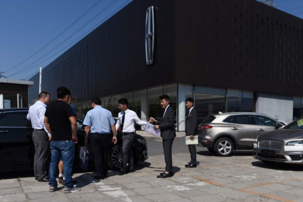 A group of people talk with salesmen outside a Lincoln automobile dealership in Beijing on August 23, 2018.China on August 23 said it would continue to 'counter-attack' as Washington imposed new tariffs on 16 billion USD worth of its goods, further inflaming trade tensions. / AFP PHOTO / WANG ZHAO