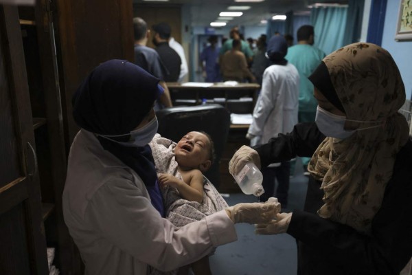 A nurse holds a Omar al-Hadidi, who was pulled alive from under the rubble while seven other family members perished, at Al-Shifa Hospital, after an Israeli air strike struck al-Shati Refugee Camp without advance warning during the night, in Gaza City early on May 15, 2021. - Israel faced a widening conflict on May 14, as deadly violence erupted across the West Bank amid a massive aerial bombardment in Gaza and unprecedented unrest among Arabs and Jews inside the country. The West Bank clashes, described as among the most intense since the second intifada that began in 2000, left 11 people dead from Israeli fire, the Palestinian health ministry said, as overall fatalities from strikes on Gaza rose to 126. (Photo by MAHMUD HAMS / AFP)