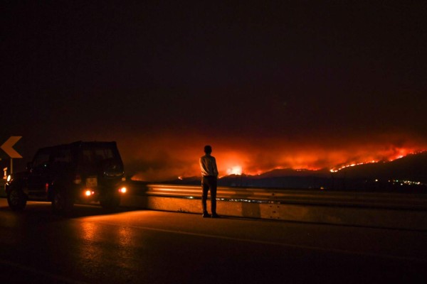 A man stands on the roadside watching a wildfire at Anciao, Leiria, central Portugal, on June 18, 2017. A wildfire in central Portugal killed at least 25 people and injured 16 others, most of them burning to death in their cars, the government said on June 18, 2017. Several hundred firefighters and 160 vehicles were dispatched late on June 17 to tackle the blaze, which broke out in the afternoon in the municipality of Pedrogao Grande before spreading fast across several fronts. / AFP PHOTO / PATRICIA DE MELO MOREIRA