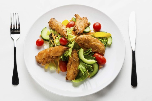 Tandoori chicken salad, with cherry tomatoes, cucumber, sweet yellow bell peppers and lettuce, laid out and ready to eat.