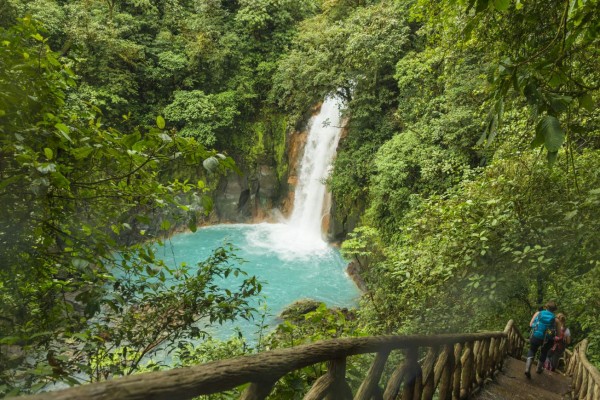 Two young woman going down a wooden stairs at the waterfall of river Celeste. River has beautiful turquoise color in the rain forest. River Celeste in Tenorio Volcano National Park, Costa Rica.