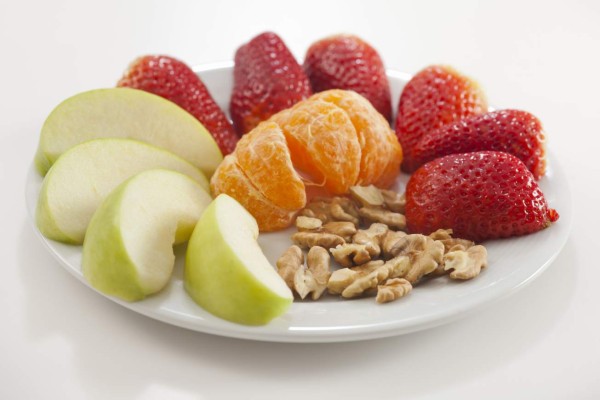 Healthy fruit snacks on a white plate. Slice apples and strawberries, walnuts and peeled tangerine. Photographed on a white background.