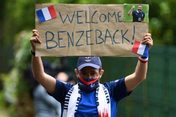 TV host Pierre-Antoine Damecour holds a placard welcoming French forward Karim Benzema, as he and other players arrive at the French national football team training base in Clairefontaine-en-Yvelines on May 26, 2021, as part of the team's preparation for the upcoming Euro-2020. (Photo by FRANCK FIFE / AFP) / The erroneous mention[s] appearing in the metadata of this photo by FRANCK FIFE has been modified in AFP systems in the following manner: [TV host Pierre-Antoine Damecour] instead of [A fan ]. Please immediately remove the erroneous mention[s] from all your online services and delete it (them) from your servers. If you have been authorized by AFP to distribute it (them) to third parties, please ensure that the same actions are carried out by them. Failure to promptly comply with these instructions will entail liability on your part for any continued or post notification usage. Therefore we thank you very much for all your attention and prompt action. We are sorry for the inconvenience this notification may cause and remain at your disposal for any further information you may require.