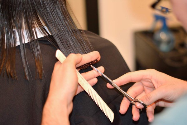 Young woman at the hair stylist, close up wet hair, comb and hairdressers hands.
