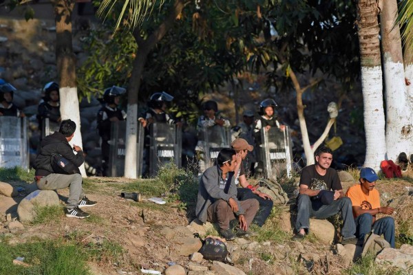 Central American migrants -heading in a caravan for the US- rest next to a line of Mexican police on the bank of the Suichate River, where they spent the night, in Ciudad Hidalgo, Mexico, after crossing from Tecum Uman, Guatemala, on January 21, 2020. - Some 500 Central Americans, from the so-called '2020 Caravan', crossed Monday from Guatemala to Mexico, but over 400 were intercepted when National Guardsmen fired tear gas at them. (Photo by ALFREDO ESTRELLA / AFP)