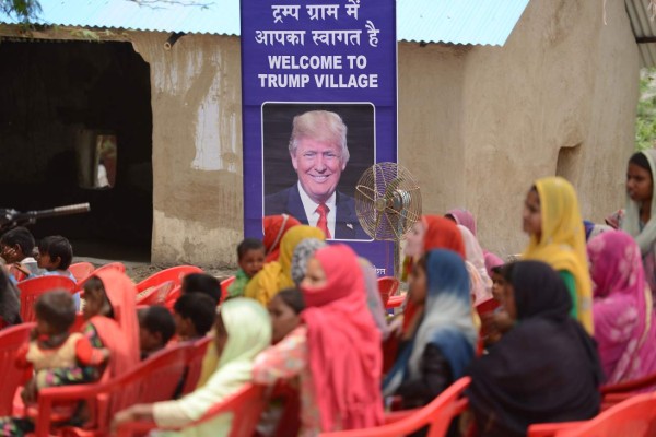 Indian women gather to listen to a speaker next to a poster with the image of US President Donald Trump during a ceremony at Marora village, which has been unofficially renamed 'Trump Village,' about 100km from New Delhi, on June 23, 2017.A rural Indian settlement with little electricity or running water renamed itself 'Trump Village' on June 23 in an unusual gesture to the American president ahead of Prime Minister Narendra Modi's trip to Washington. A huge billboard declaring 'Welcome to Trump Village' in Hindi and English, accompanied with a beaming portrait of the US president, was unveiled in Haryana state's Marora, as the village is officially known. The water and sanitation group Sulabh, which has been installing toilets in the impoverished settlement, suggested the name change to the local council. / AFP PHOTO / MONEY SHARMA