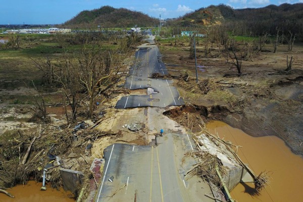 A man rides his bicycle through a damaged road in Toa Alta, west of San Juan, Puerto Rico, on September 24, 2017 following the passage of Hurricane Maria.Authorities in Puerto Rico rushed on September 23, 2017 to evacuate people living downriver from a dam said to be in danger of collapsing because of flooding from Hurricane Maria. / AFP PHOTO / Ricardo ARDUENGO