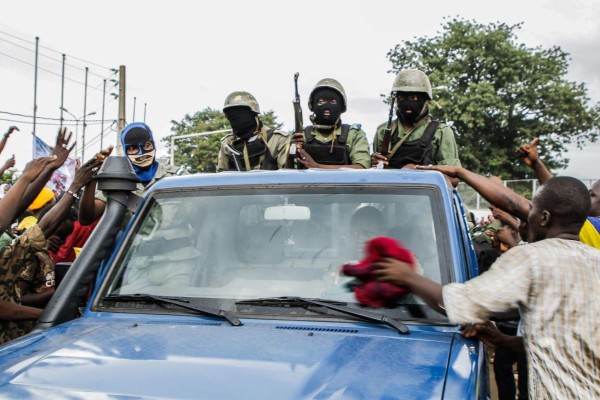 A man uses a red cloth to clean the windscreen of a pick up truck carrying armed masked Malian soldiers as they arrive at Independence Square in Bamako on August 18, 2020. - Rebel troops seized Malian President Ibrahim Boubacar Keita and Prime Minister Boubou Cisse in a dramatic escalation of a months-long crisis on August 18. Neighbouring states in West Africa, along with France, the European Union and the African Union, condemned the sudden mutiny and warned against any unconstitutional change of power in the fragile country. (Photo by STRINGER / AFP)