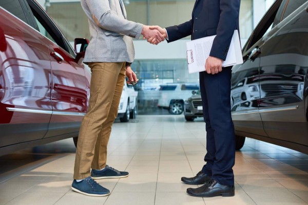 Low section side view of handsome client shaking hands with sales manager in car showroom, after buying brand new luxury car