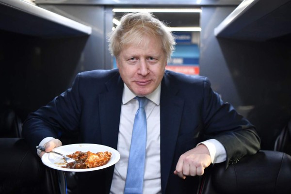 TOPSHOT - Britain's Prime Minister Boris Johnson eats a portion of pie on the campaign bus after a visit to the Red Olive catering company in Derby, central England on December 11, 2019 while on the campaign trail. - Britain will go to the polls tomorrow to vote in a pre-Christmas general election. (Photo by Ben STANSALL / various sources / AFP)