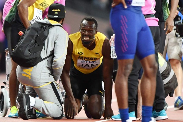 Jamaica's Usain Bolt (C) receives attention on the track after pulling up injured in the final of the men's 4x100m relay athletics event at the 2017 IAAF World Championships at the London Stadium in London on August 12, 2017. / AFP PHOTO / Jewel SAMAD