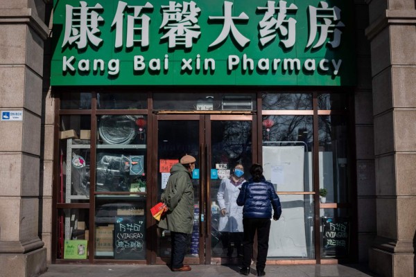 People wearing protective facemasks and gloves stand outside a closed off Pharmacy as they try to get facemasks, gloves and hand sanitiser gel in Beijing on February 15, 2020. - The death toll from the new coronavirus outbreak jumped past 1,500 in China as France reported the first fatality outside Asia, fuelling global concerns about the epidemic (Photo by NICOLAS ASFOURI / AFP)