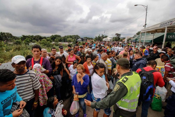 Venezuelans gather in front of a Colombian policeman as they attempt to cross the Simon Bolivar international bridge, in Cucuta, Colombia, in the border with Venezuela on April 2, 2019. - After the level of the Tachira River rose, the 'trochas' -illegal trails- were flooded and Venezuelans who needed to cross to Colombia and back, climbed containers and walked through the blocked Simon Bolivar bridge in a desperate attempt to go through. (Photo by Schneyder MENDOZA / AFP)