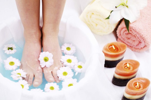 Woman's legs in blue water on spa treatment surrounded by towels and candles.