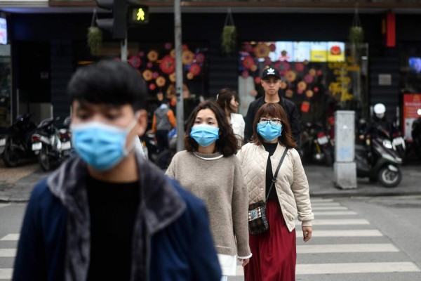 Pedestrians, wearing protective facemasks amid concerns of the novel coronavirus outbreak, cross a street in Hanoi on February 7, 2020. (Photo by Manan VATSYAYANA / AFP)