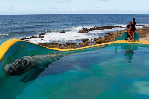 A couple stand on the ledge of a makeshift pool in the neighbourhood of La Perla where the video 'Suavecito' was recorded in San Juan, on July 22, 2017.Something unusual is happening in La Perla, a poor barrio clinging to a steep hillside between Old San Juan and the sea where the video for the pop hit 'Despacito' was filmed. / AFP PHOTO / Ricardo ARDUENGO
